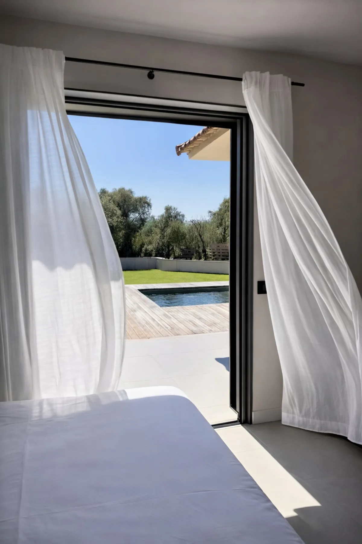 Vue depuis la chambre vers la piscine privative à travers les rideaux blancs